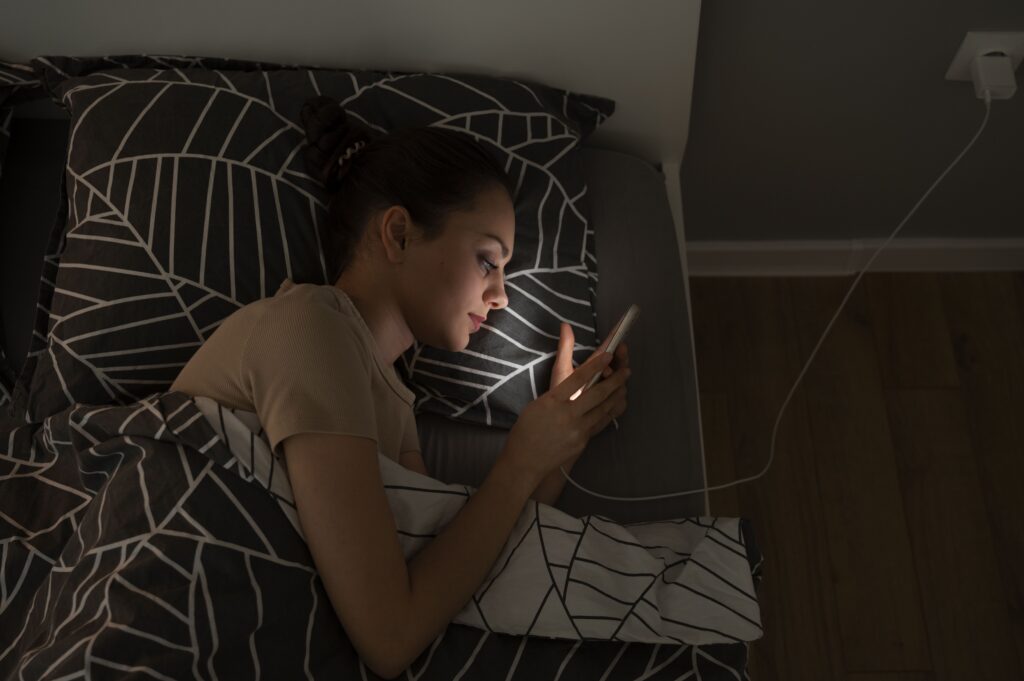 Vue de dessus fille allongée dans son lit avec smartphone
